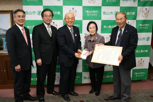 源さんが「第1回畑崎記念ファッショナブルエージング賞」の副賞の賞金一部を市長へ手渡し、職員の方と一緒に記念撮影している写真